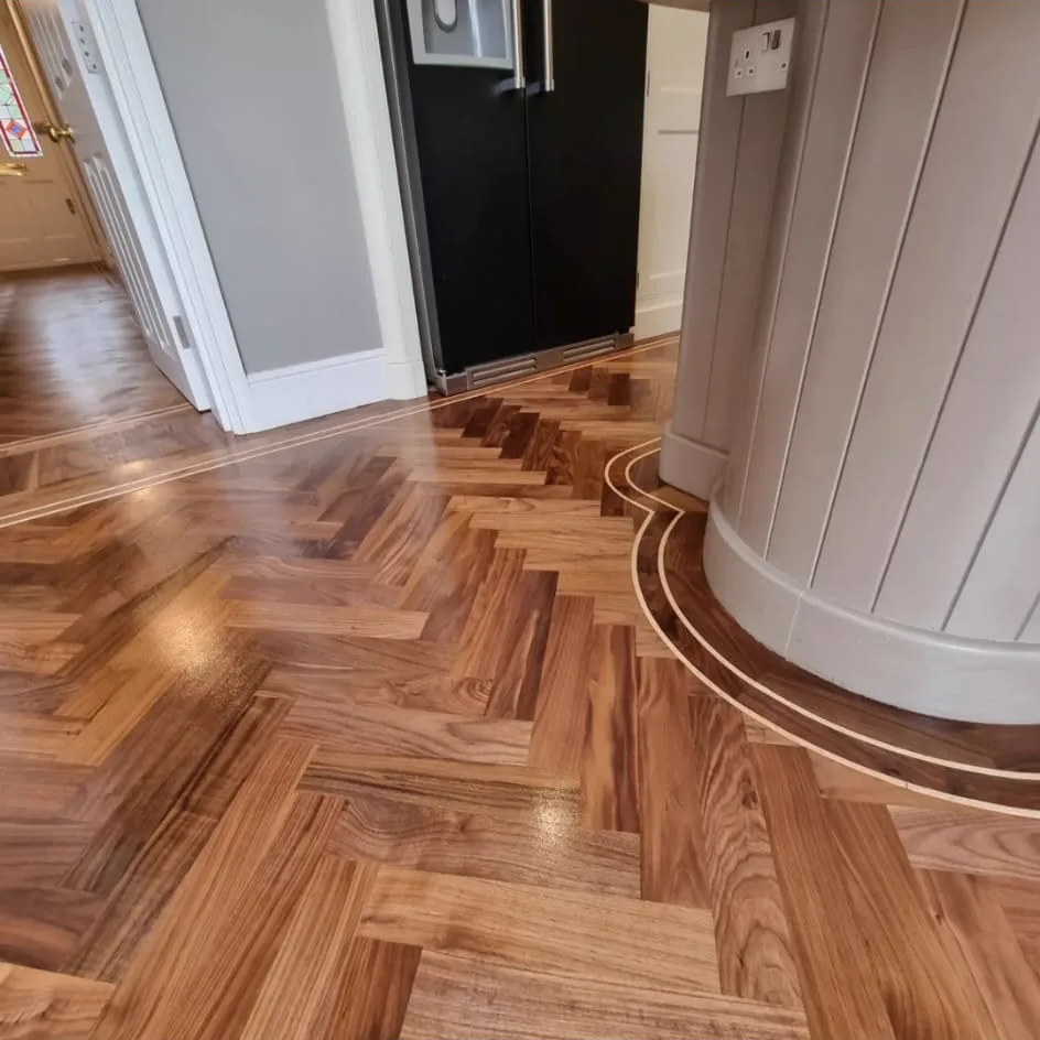 Double inlay border sweeping around a kitchen island on a Fulham SW6 walnut herringbone floor