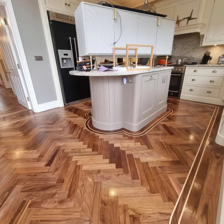 Restored walnut herringbone floor with a double inlay border curving around a kitchen island in Fulham SW6, by Howard Naish