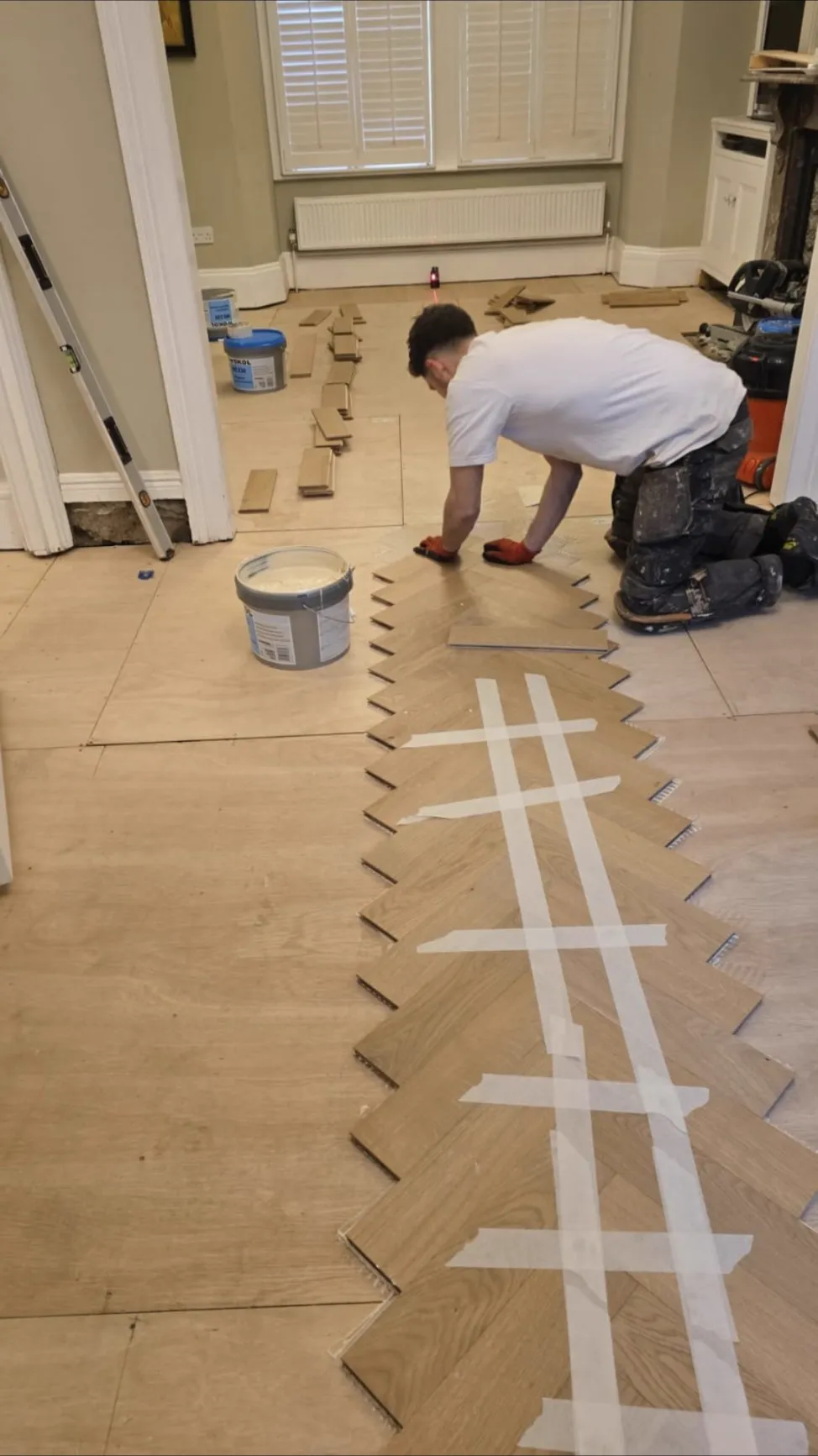 Luke Howard kneeling on a prepared subfloor, laying the centre spine of an oak herringbone floor on a laser line