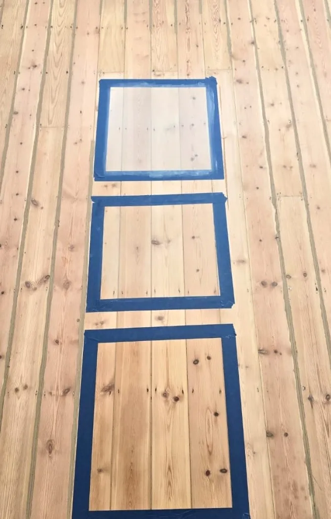 Patch test on a sanded pine floor showing three taped squares finished with one, two and three coats of white