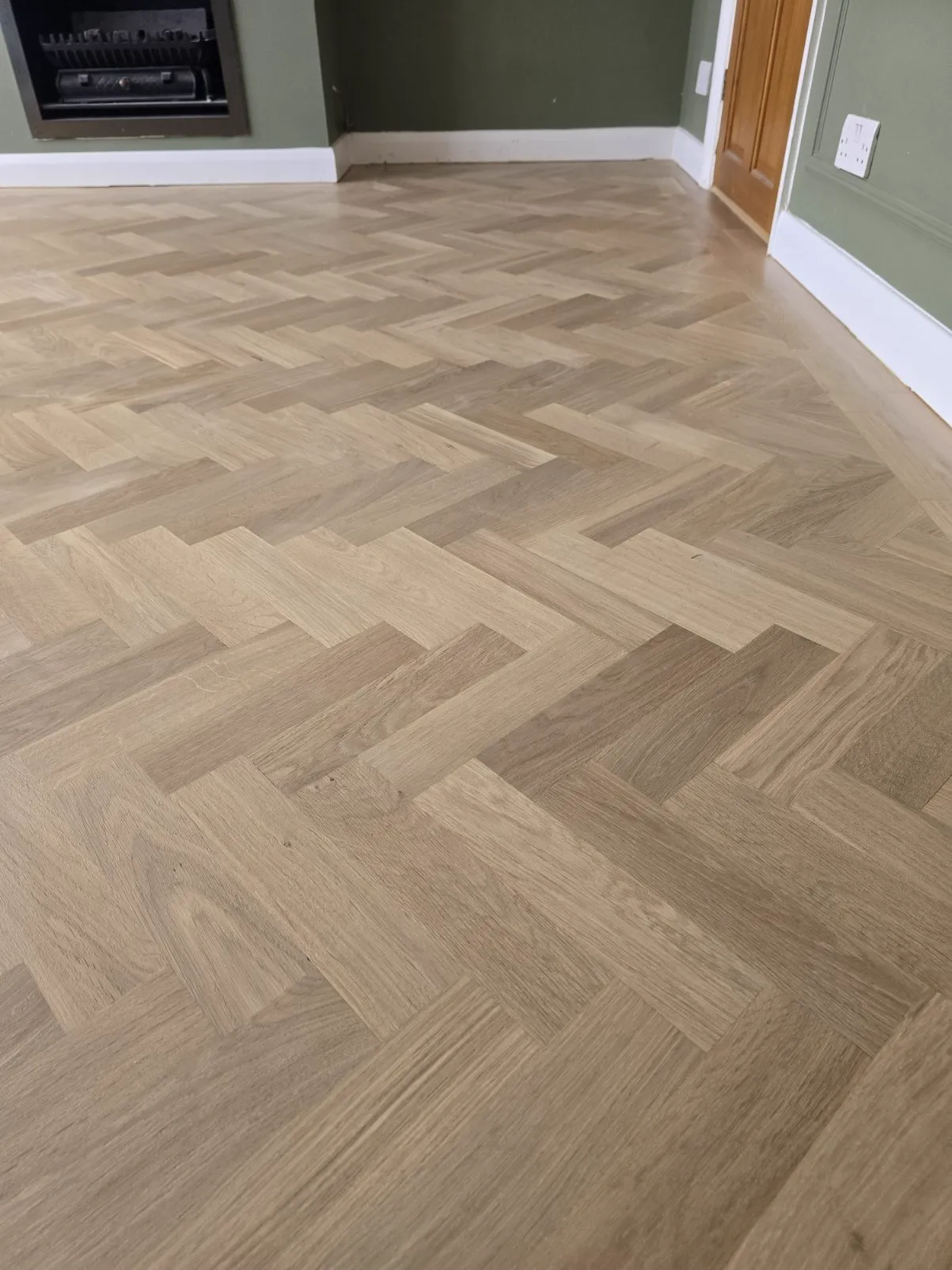 Close-up of oak herringbone blocks around a fireplace in a Purley CR8 sitting room, re-bonded and refinished by Howard Naish