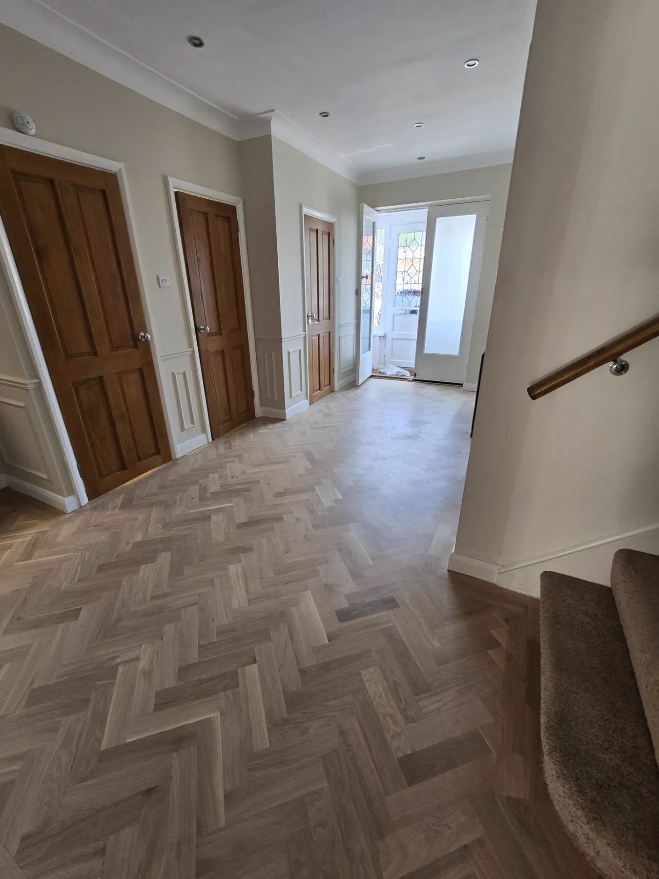 Oak herringbone parquet running through a 1930s Purley hallway with stained glass front door, restored by Howard Naish