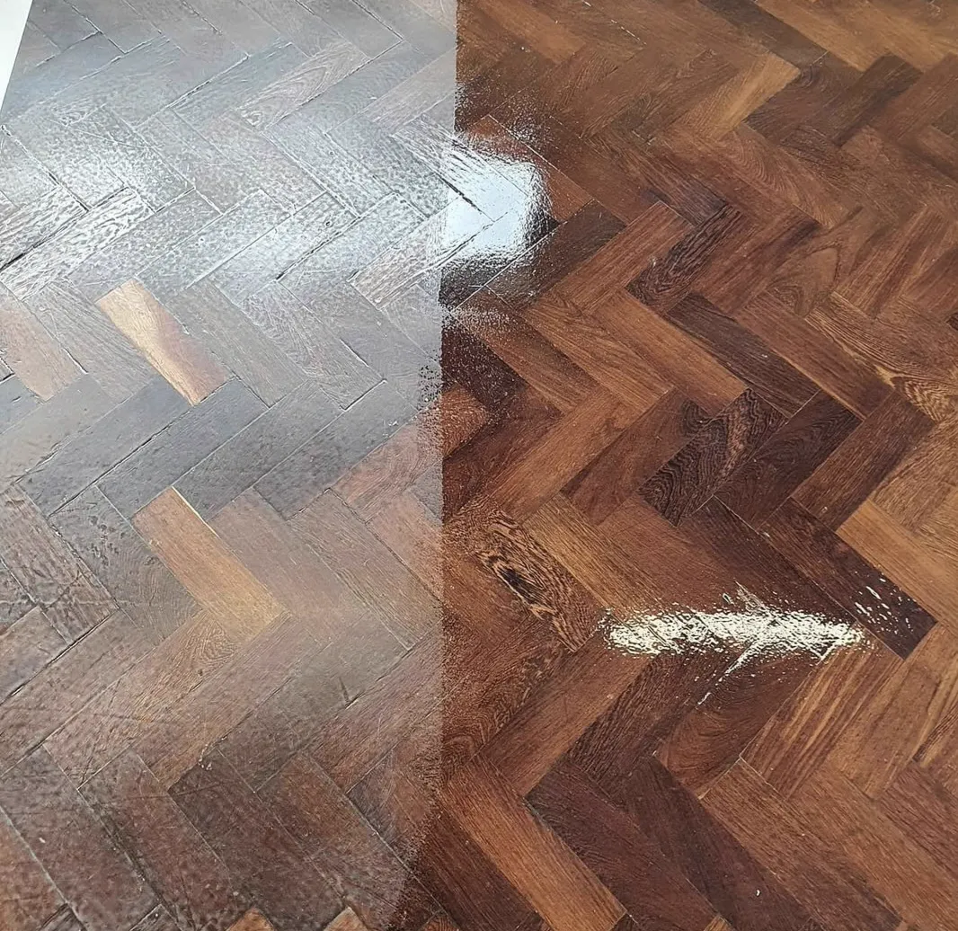 Close-up of the same Scout hall parquet mid-recoat: dull worn finish on the left, fresh glossy finish on the right