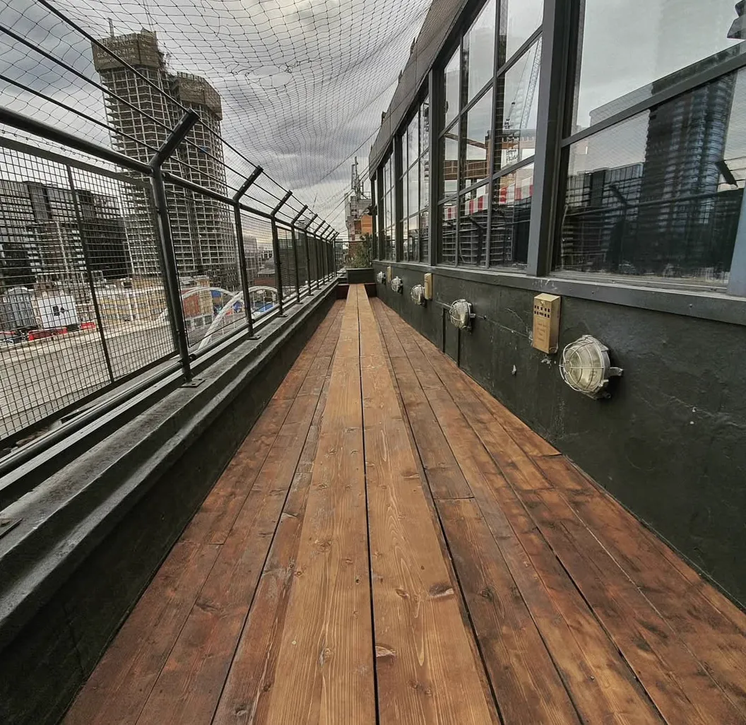 Restored timber roof deck at Shoreditch House with the city skyline behind, sanded and oiled by Howard Naish